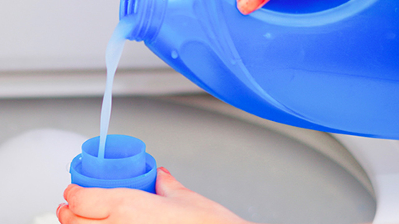 Person pouring liquid detergent into dosing cup